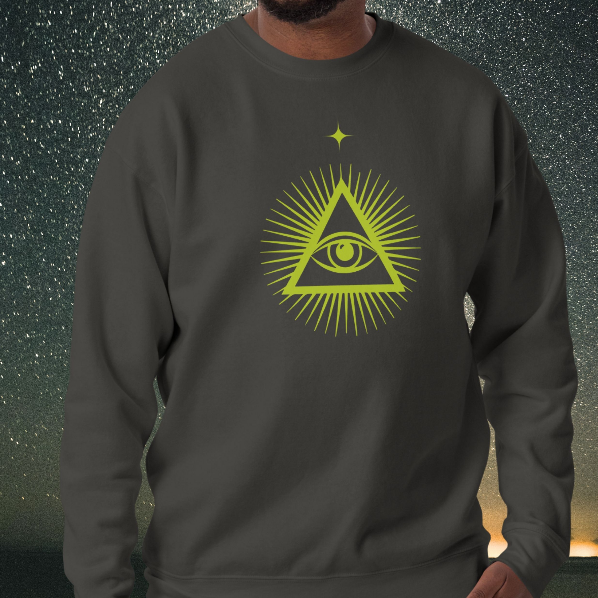 Person wearing a dark gray Stellarwear sweatshirt with a green triangle symbol featuring an eye design against a starry night sky background.