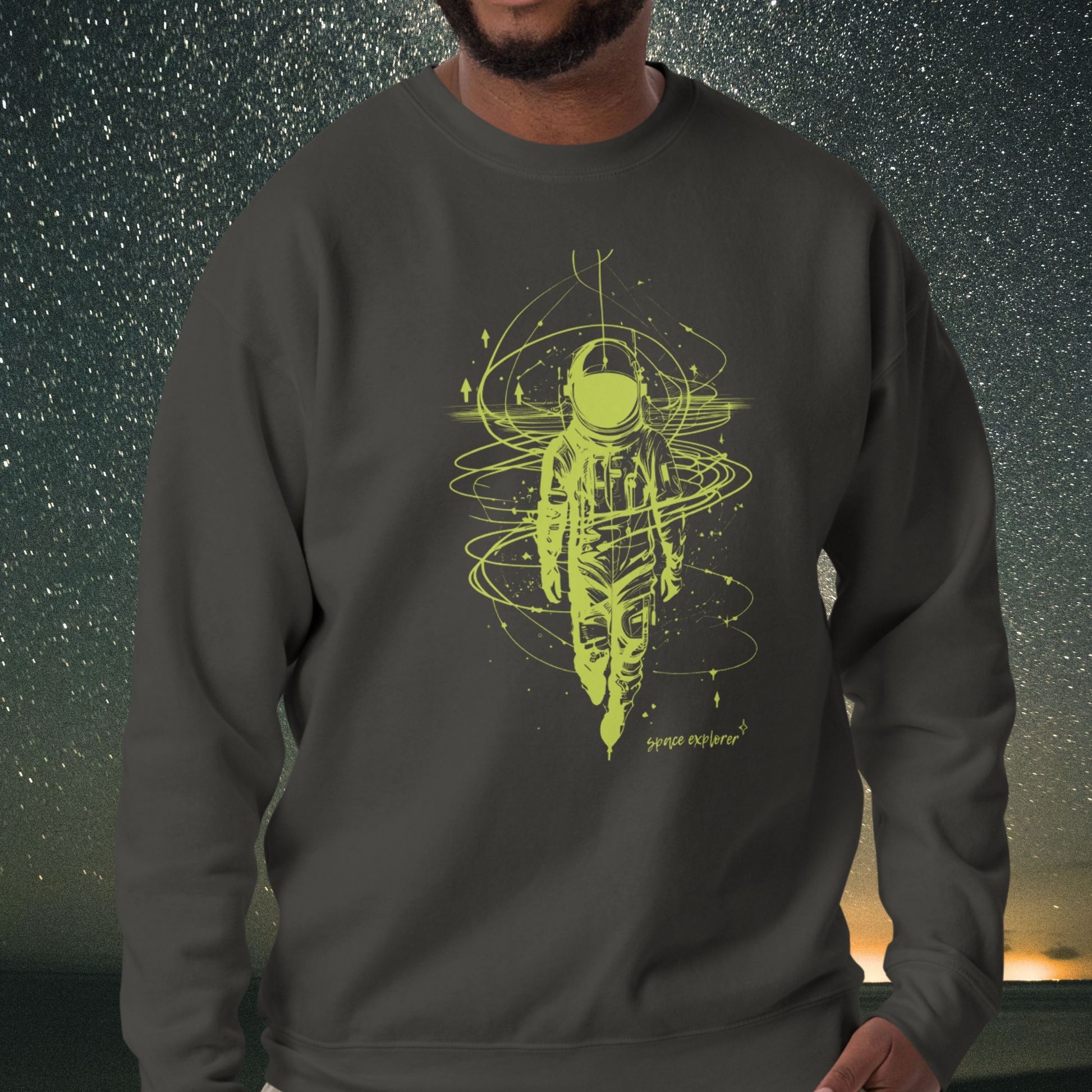 Person wearing a dark gray Stellarwear sweatshirt with a green astronaut design against a starry night sky.