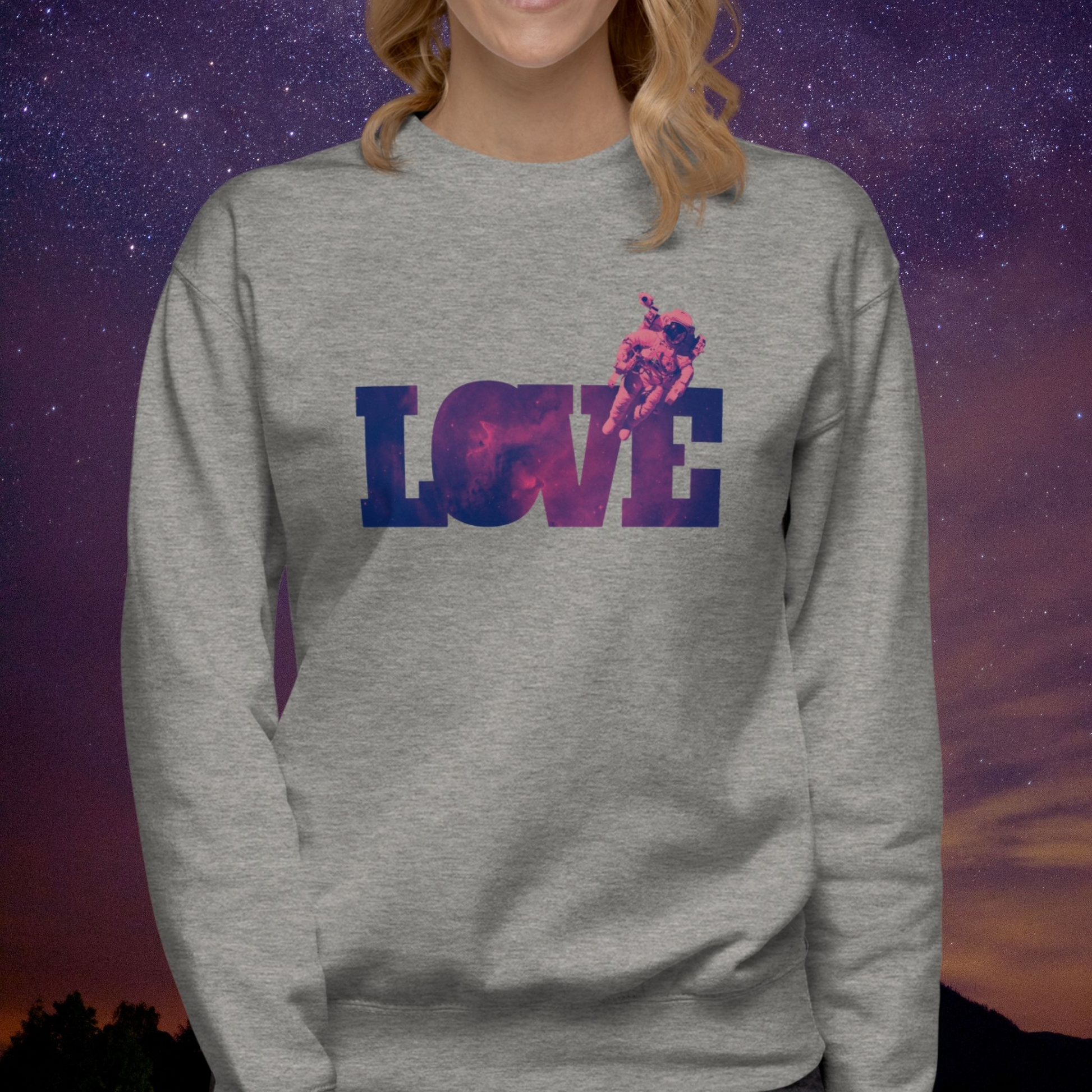 Person wearing a gray Stellarwear sweatshirt with 'LOVE' astronaut graphic design against a starry sky background