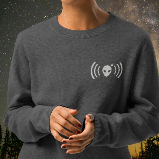 Person wearing a charcoal Stellarwear sweater with a white alien graphic design against a starry night sky background