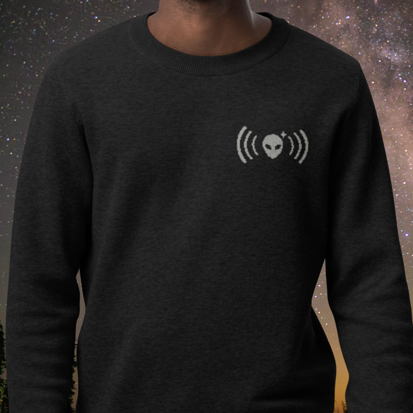 Black Stellarwear sweater with a white logo worn by a person against a starry night sky background