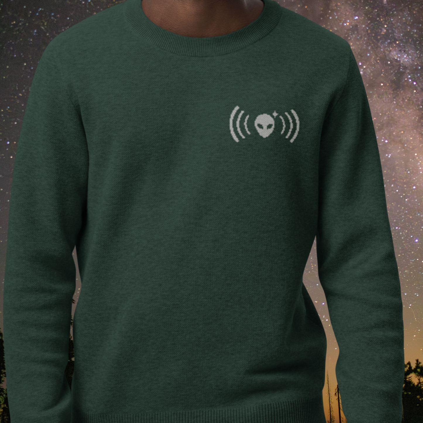 Green Stellarwear sweater with alien and radio waves design against a starry night sky background