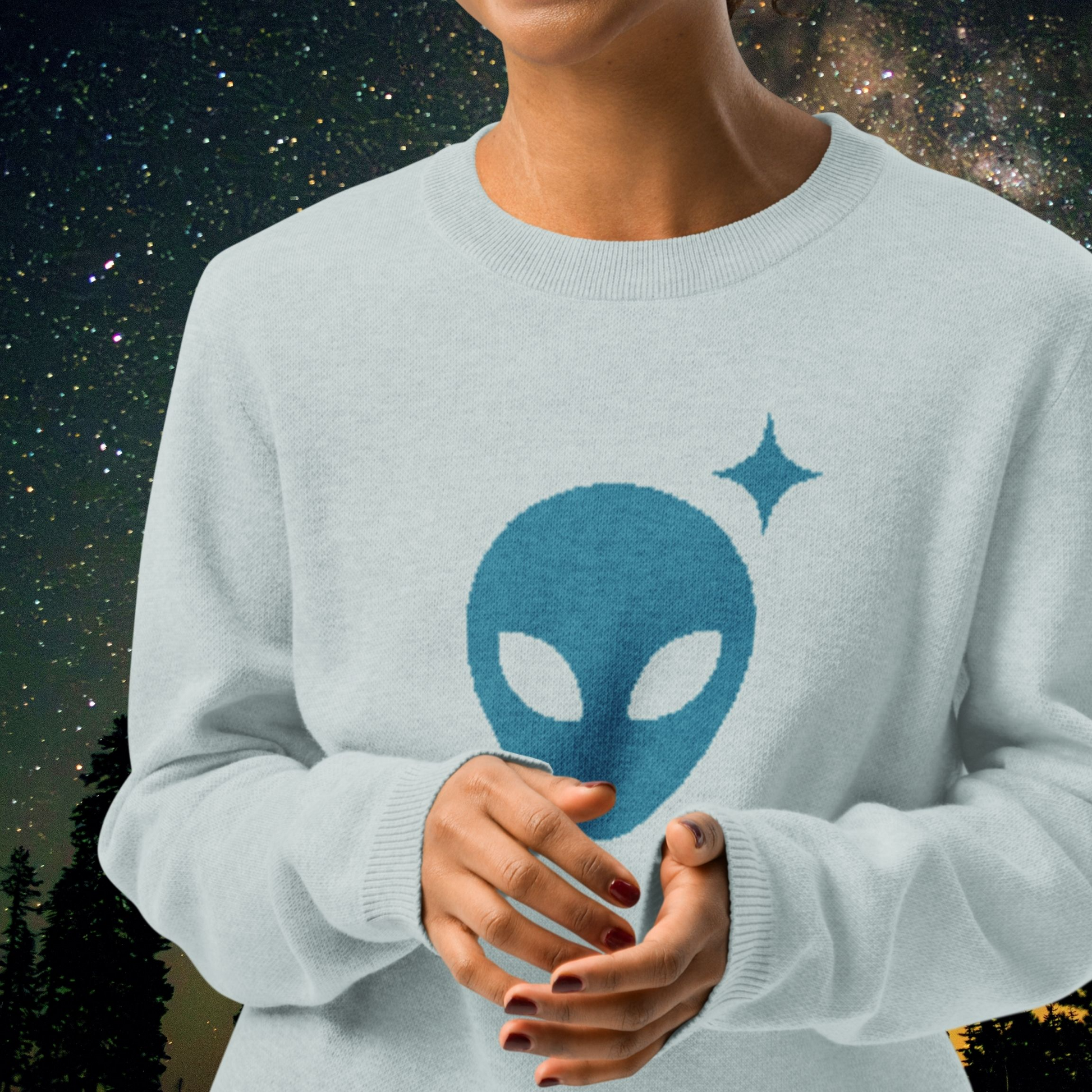 Light blue Stellarwear sweater with alien face design against a starry night sky background