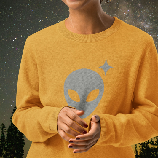 Person wearing a mustard yellow Stellarwear sweater with an alien head design against a starry night sky.