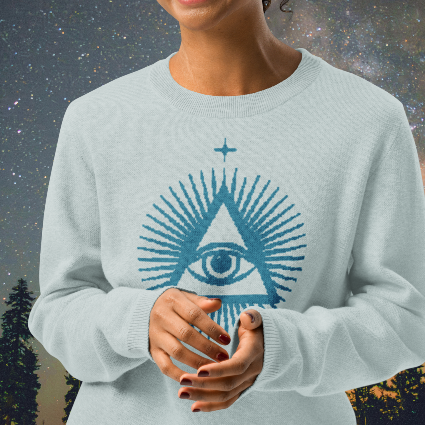 Light blue Stellarwear sweater with a star and eye design worn by a person against a blurred natural background