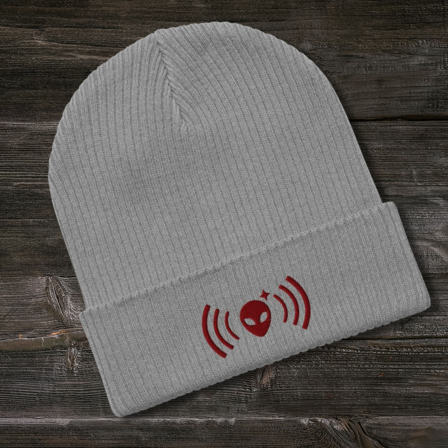 Gray Stellarwear beanie with a maroon alien and radio wave design on a wooden surface