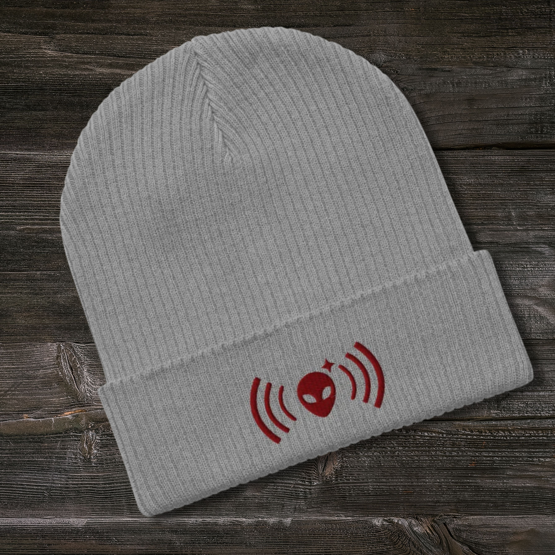 Gray Stellarwear beanie with a maroon alien and radio wave design on a wooden surface