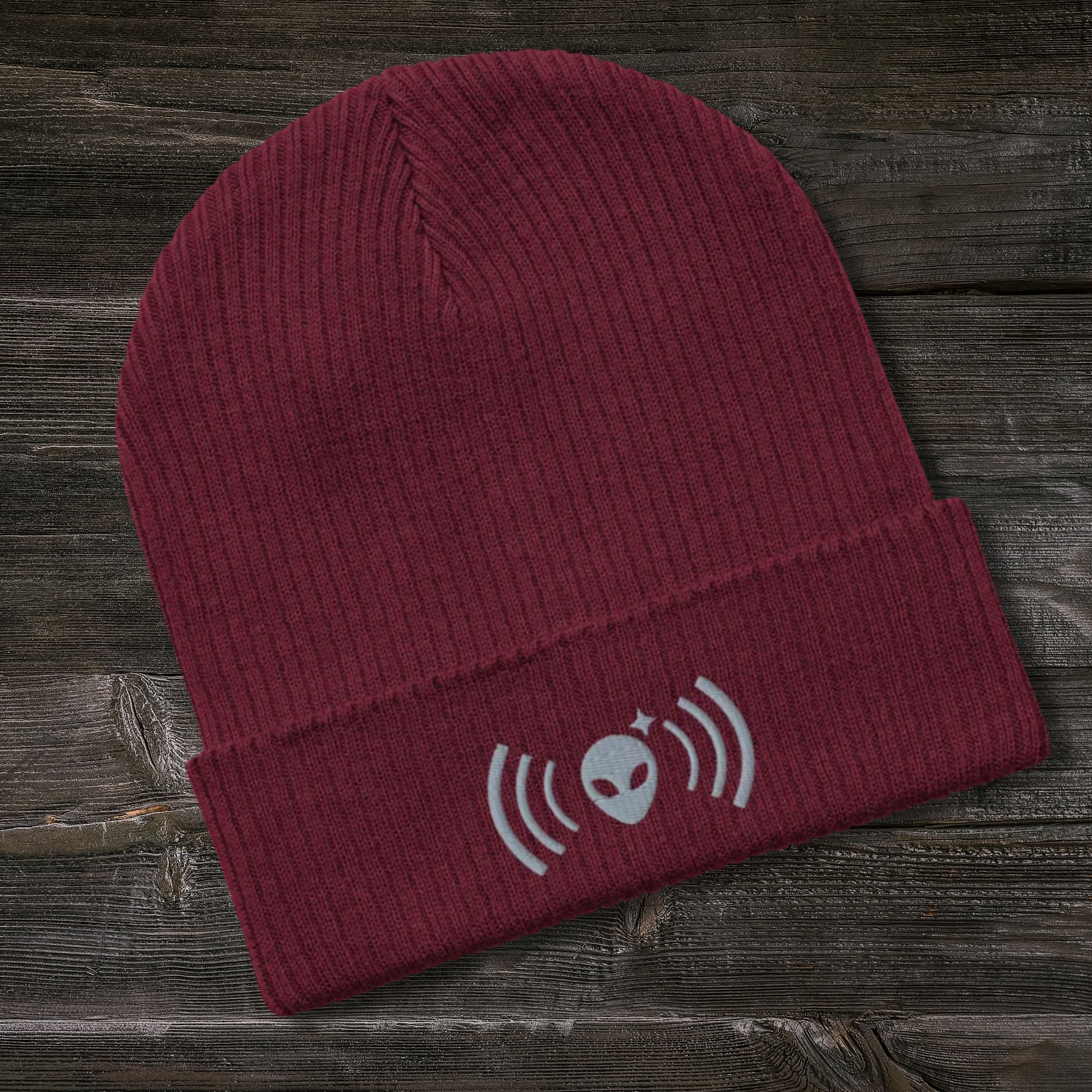 Maroon Stellarwear beanie with alien and radio wave design on a wooden surface