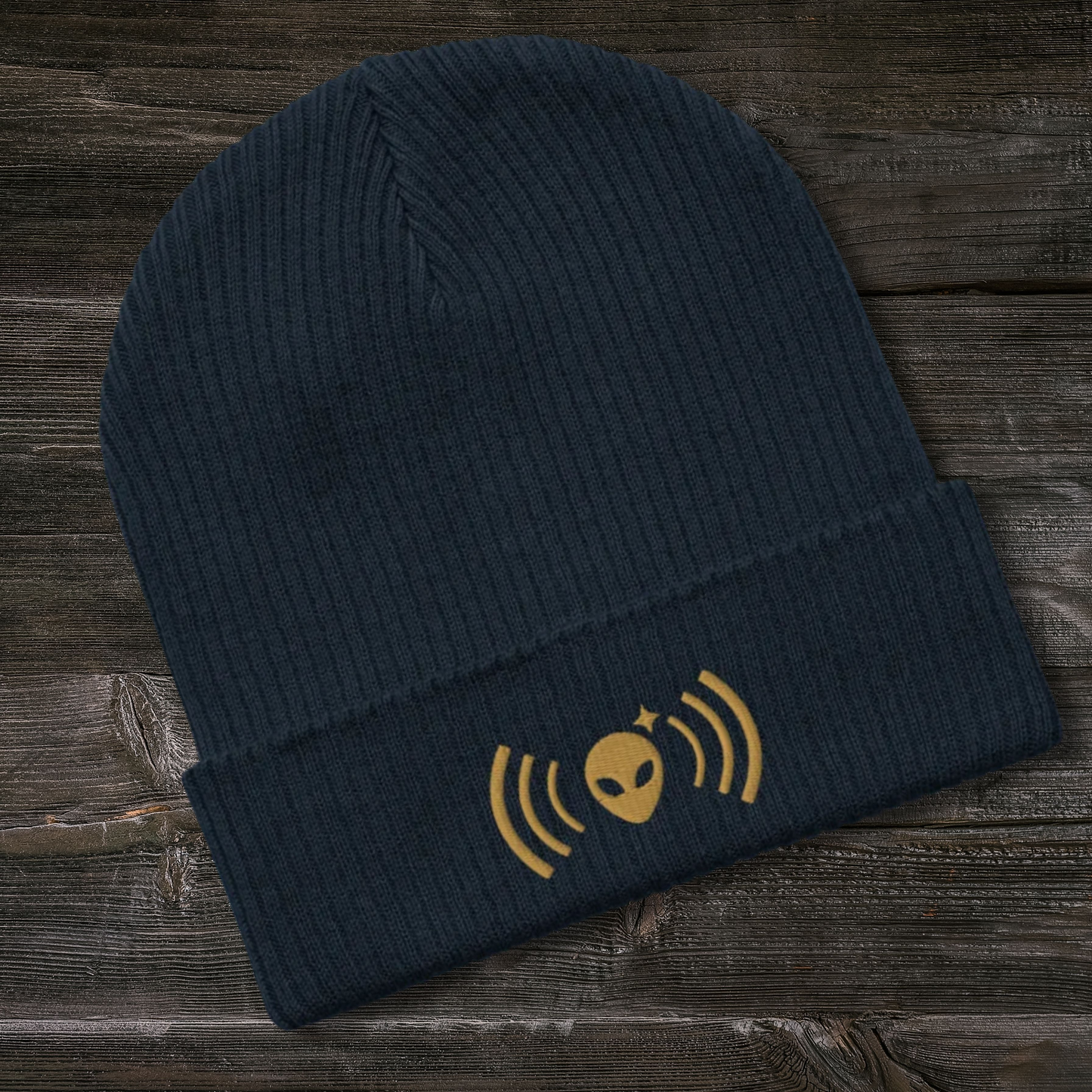 Dark blue Stellarwear beanie with gold alien and radio wave design on a wooden surface