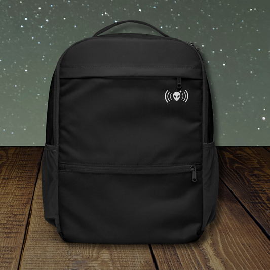Stellarwear black utility backpack with a alien signal logo on a wooden surface and starry night background
