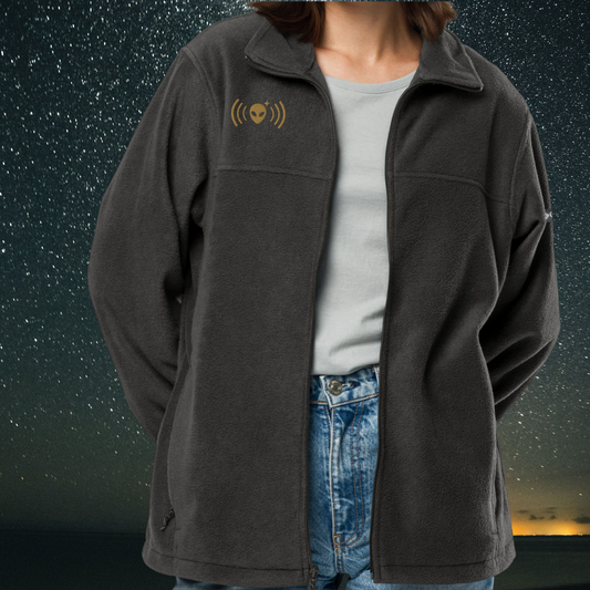Person wearing a Stellarwear dark gray jacket with an alien signal icon on the chest against a starry night sky background.