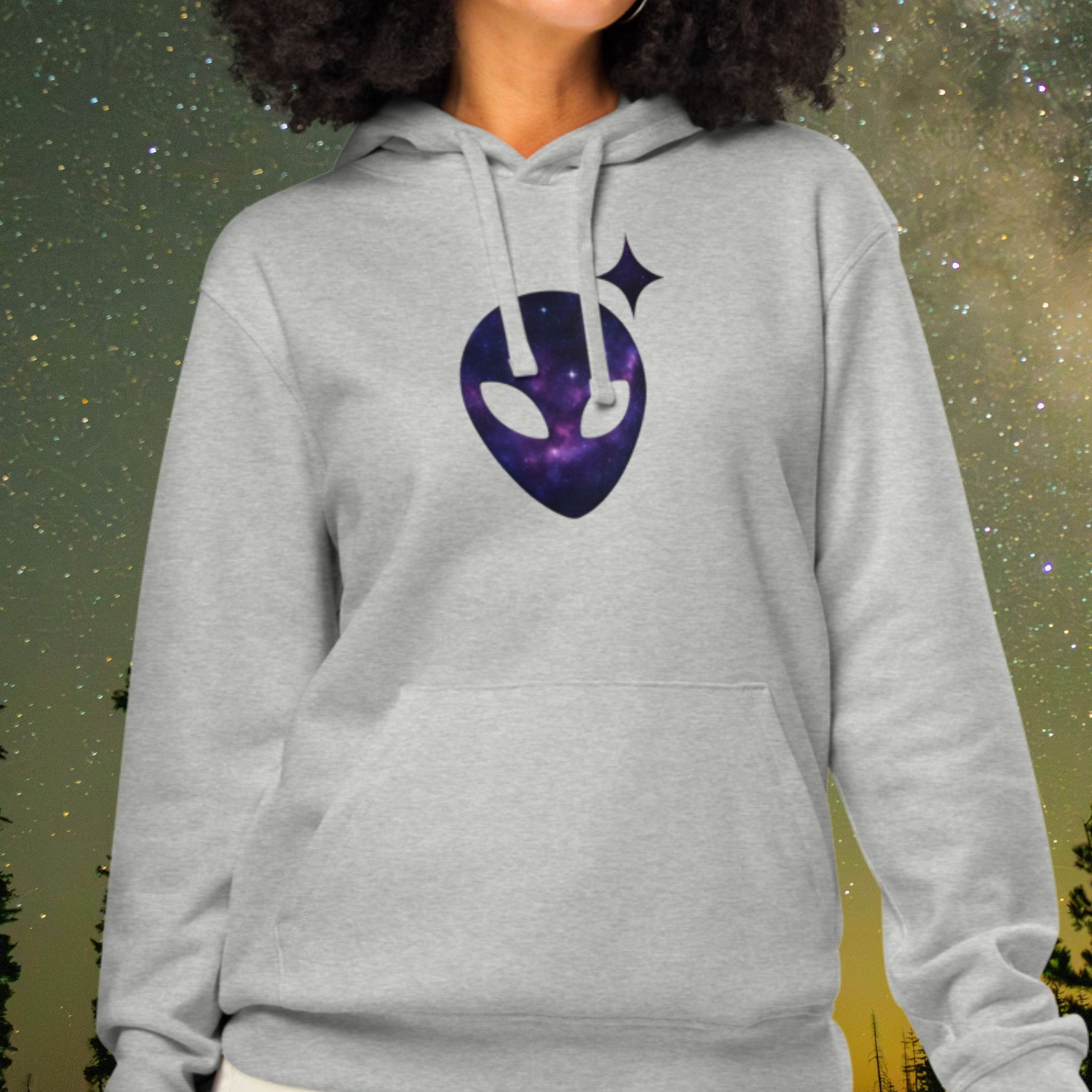 Person wearing a gray Stellarwear hoodie with a purple alien head design against a starry night sky.