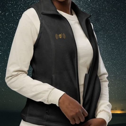 Person wearing a Stellarwear charcoal fleece vest with an alien signal embroidered in bronze against a starry night sky.