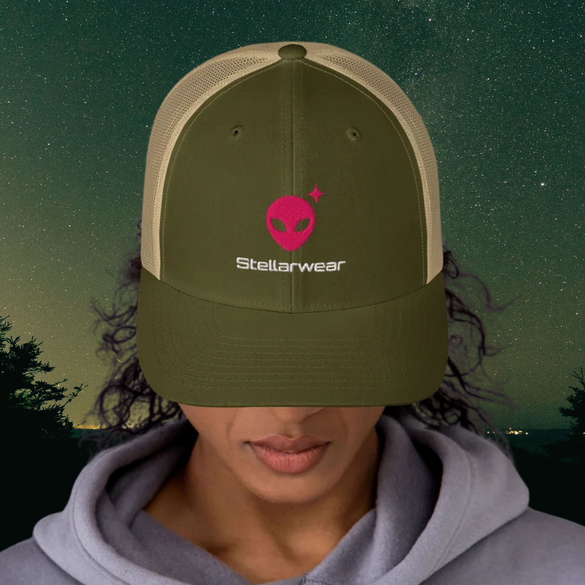 Person wearing a Stellarwear green cap with 'Stellarwear' alien logo against a night sky