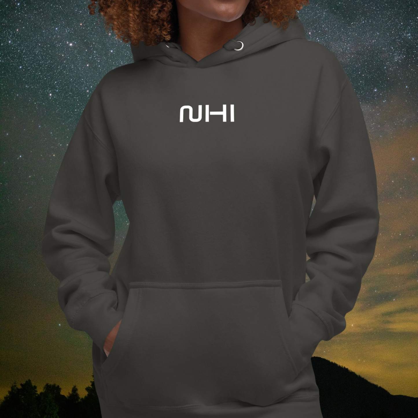 Person wearing a dark gray Stellarwear hoodie with 'NIHI' logo against a starry night sky