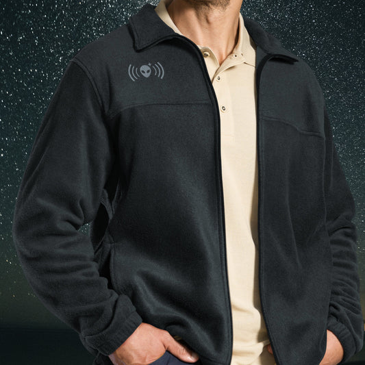 Person wearing a black Stellarwear jacket with an alien signal icon on the chest against a dark background