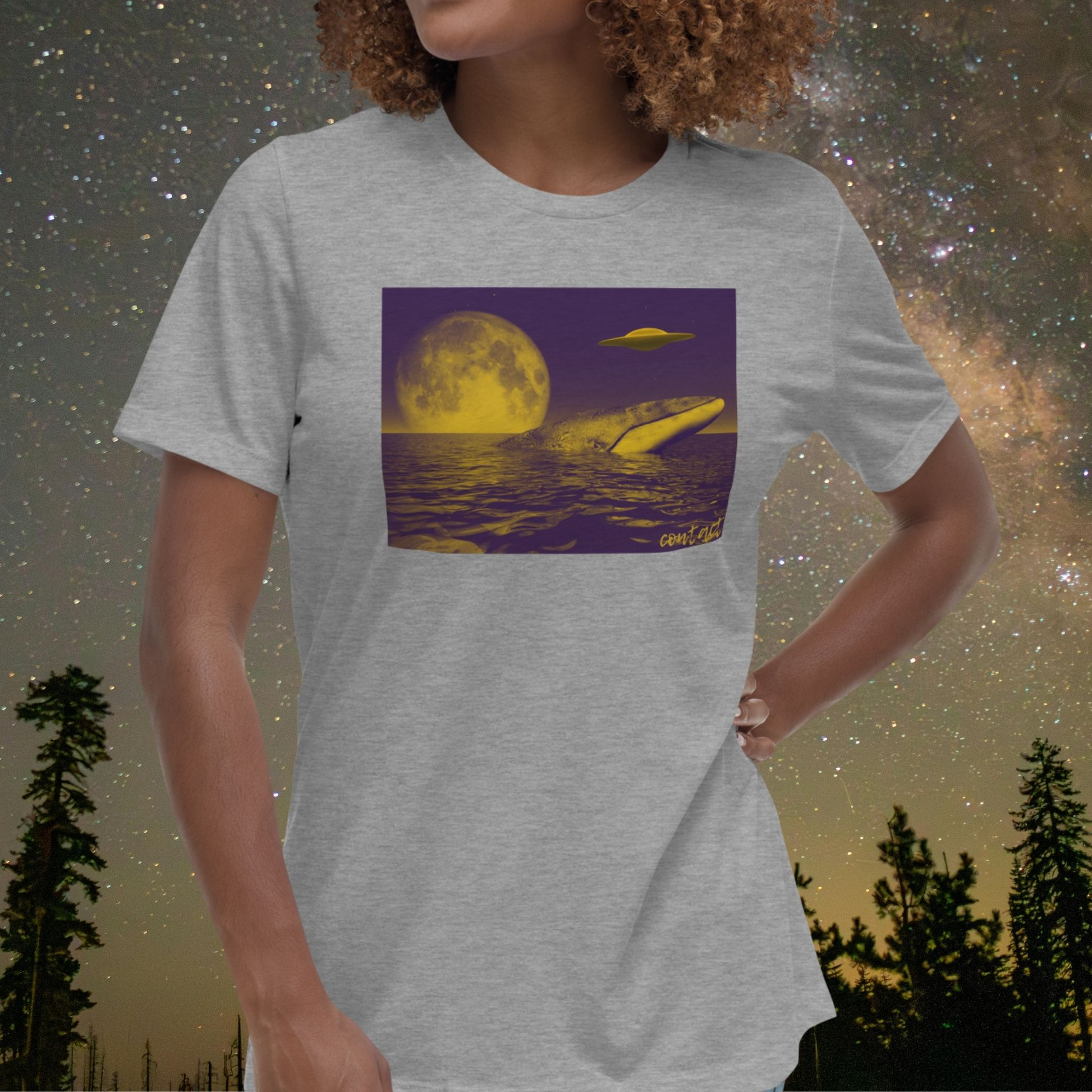 Person wearing a gray Stellarwear t-shirt with a whale, UFO and moon graphic, set against a starry night sky with trees.
